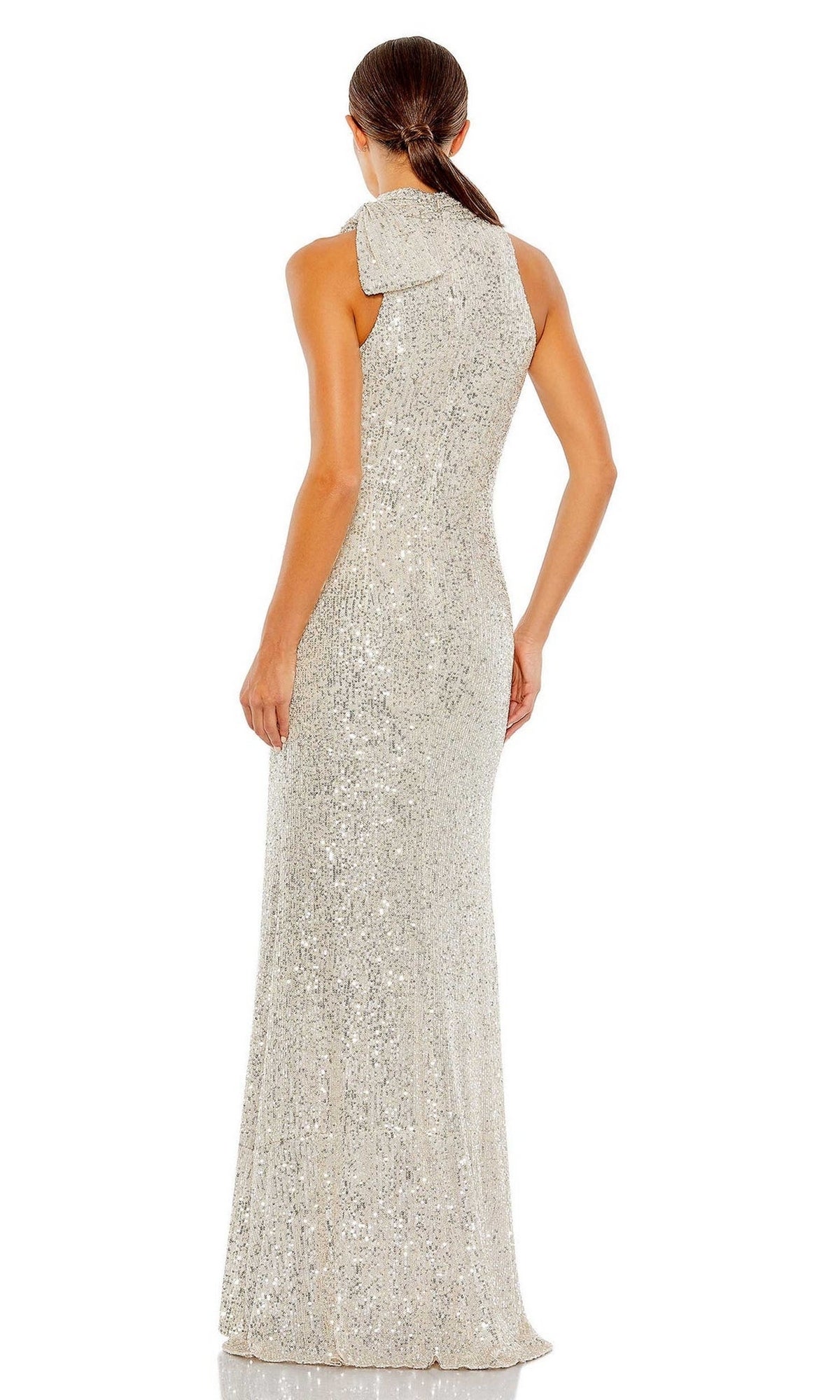 A woman stands facing away in the Mac Duggal 11280 Bow Long Sequin Formal Dress, featuring a large bow detail on one shoulder, sparkling sequins, and her hair tied back for an elegant look.
